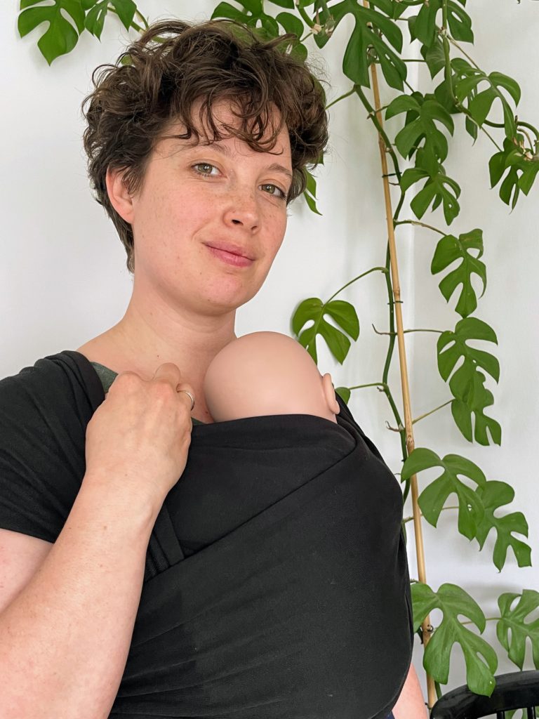 Margaux Chevalier-Vasseur, monitrice de portage physiologique porte un poupon dans une écharpe tricotée noire